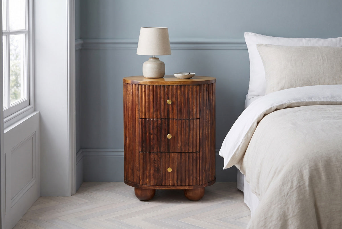 Ploaghe chestnut mango oval nightstand with a ceramic lamp in a Brooklyn bedroom with a dusty blue-grey wall and a pale herringbone floor