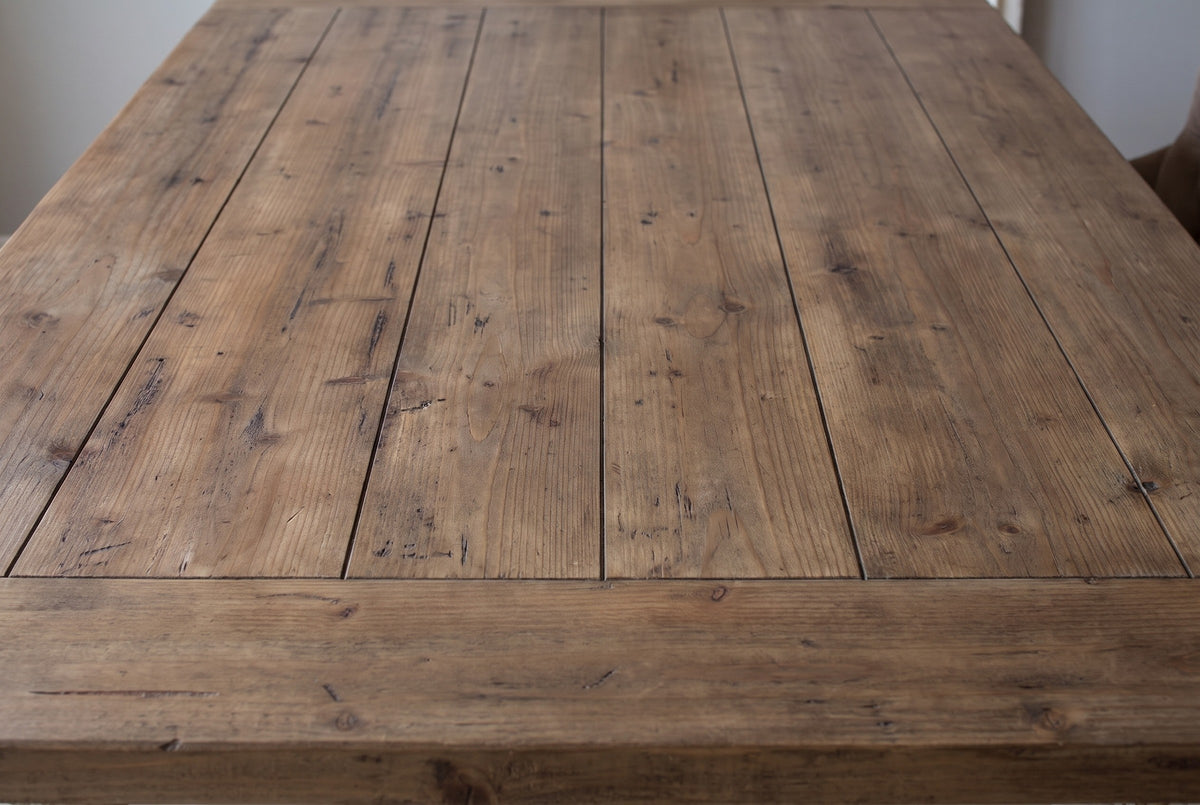 Close-up of the fir plank top of the Policoro dining table: weathered brown boards with fine seams, knots and saw marks, and the breadboard end