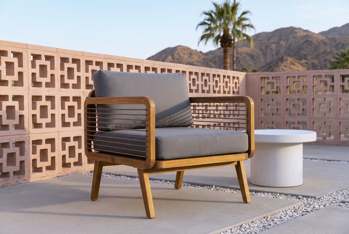 Polizzi acacia lounge armchair on concrete pavers on a Palm Springs patio at golden hour, a terracotta-pink breeze-block wall, a fan palm and the desert mountains behind (side table not included)