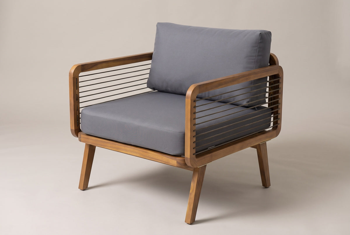 The Polizzi outdoor lounge armchair in teak-finish acacia with horizontal rope sides and charcoal grey seat and back cushions, three-quarter view on a light studio backdrop