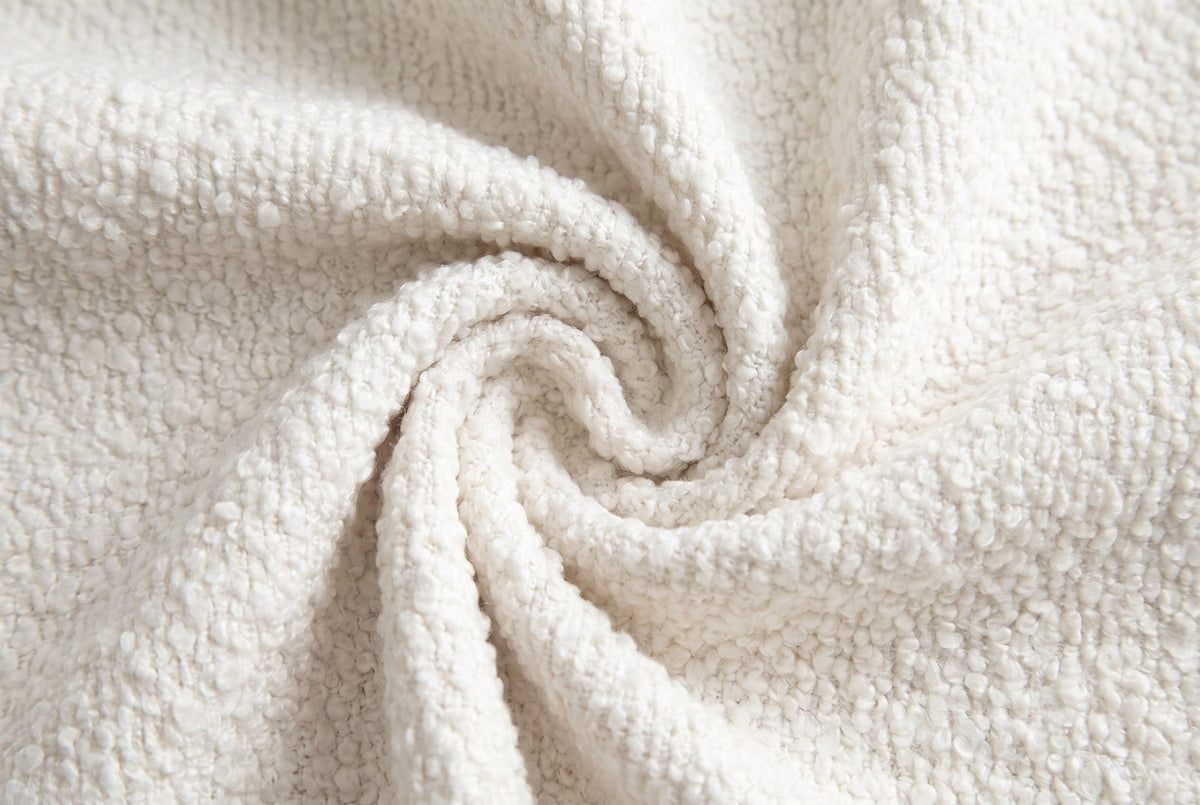 Close-up of the cream boucle on the Pollutri bed: small, curly off-white loops gathered in a soft swirl