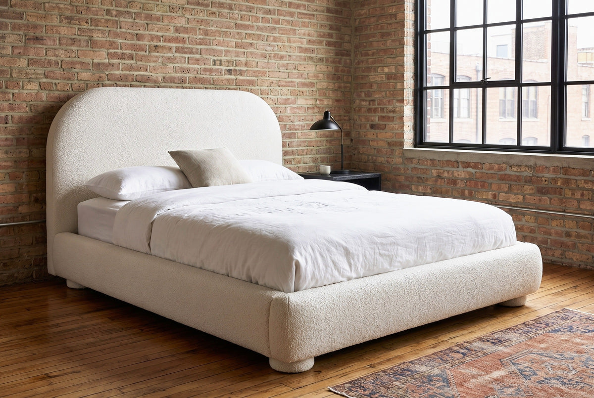 Pollutri cream boucle bed against an old red brick wall in a Chicago loft, a black steel factory window beside it