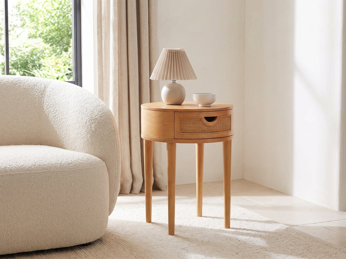 Pontedera Cane and Wood Round Side Table with a lamp and a ceramic bowl beside a cream boucle armchair in a bright plaster room