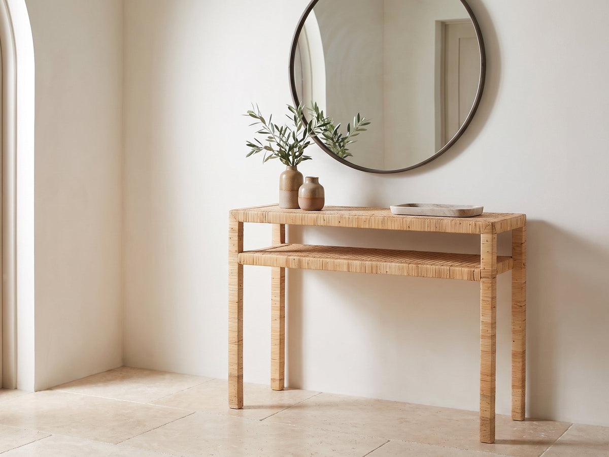 Putignano Wrapped Rattan Two-Tier Console Table under a round mirror in a travertine entryway