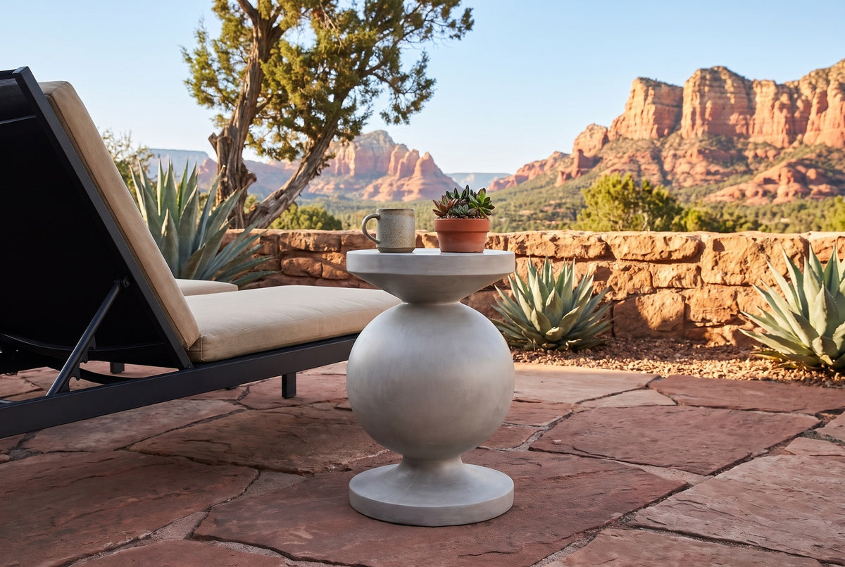 Raffadali concrete sphere pedestal side table with a stoneware mug and a pot of succulents beside a sling lounger on a red flagstone patio in Sedona, Arizona, a sandstone wall, agaves and red rock buttes behind (lounger and decor not included)