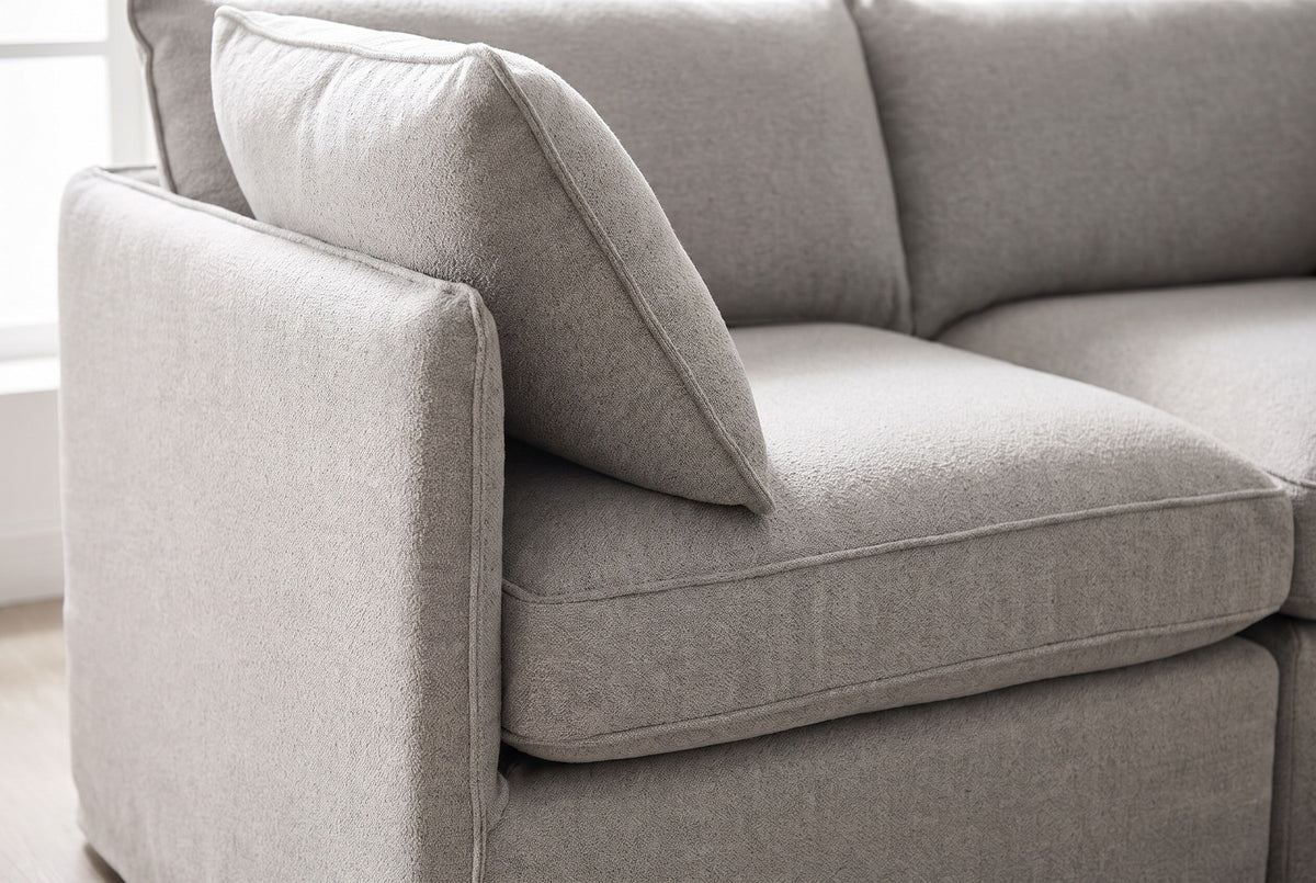 Close-up of the textured light grey fabric on a Randazzo end seat: the slim arm, an angled pillow and the piped seat cushion