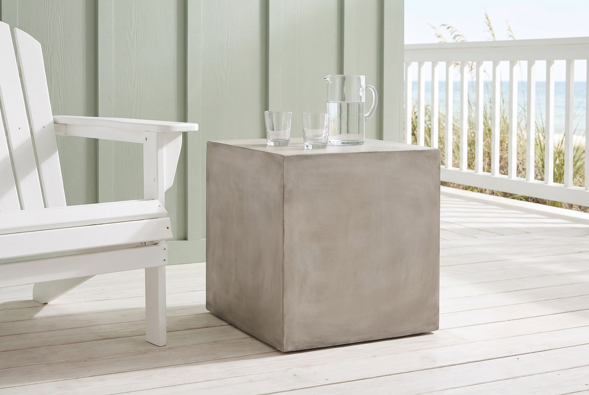 Realmonte concrete cube side table with a water jug and glasses on a beach-house porch in Seaside, Florida, a sage-green board wall and the Gulf beyond (chair and decor not included)