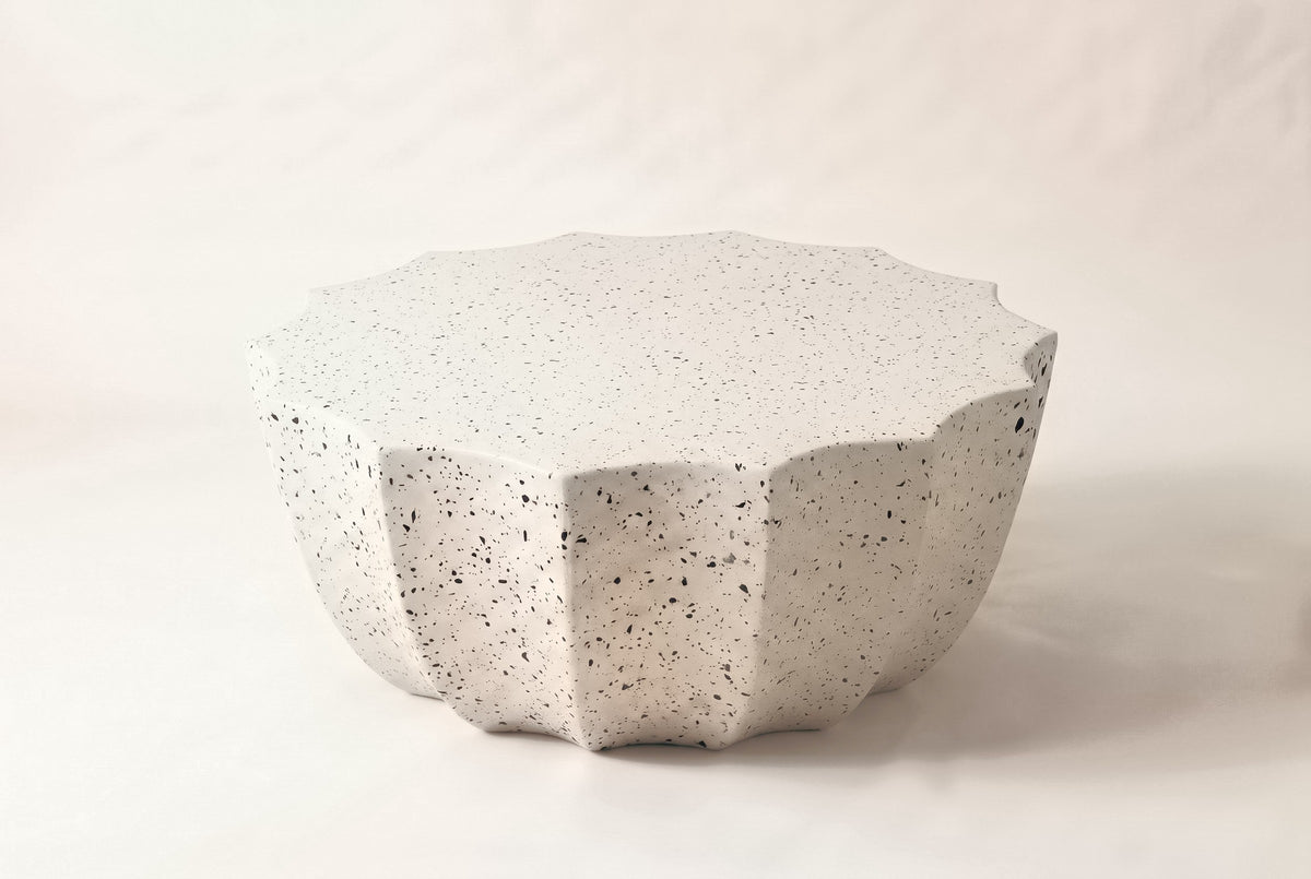 The Ribera outdoor coffee table in speckled white MgO cement with dark flecks: a 14-point scalloped round top over a fluted bowl-shaped body, on a light studio backdrop