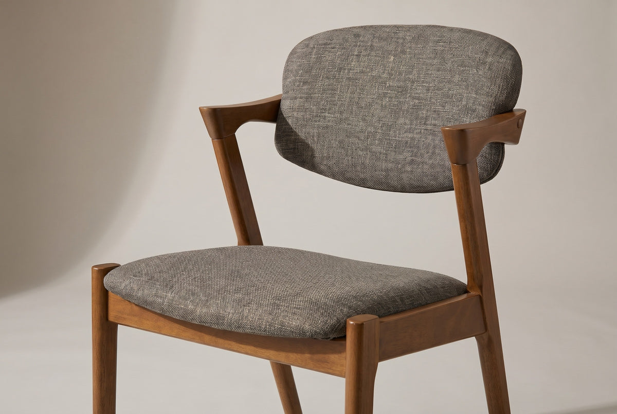 A Rossano chair in close-up: the rounded back pad in grey-brown woven fabric held by two short walnut-finished arms, and the upholstered seat on a plain wooden frame