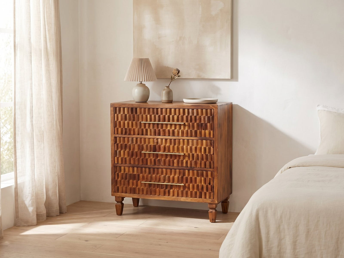 Rovigo 33-Inch Chestnut Carved Mango 3-Drawer Chest against a plaster wall under an abstract canvas in a bright bedroom