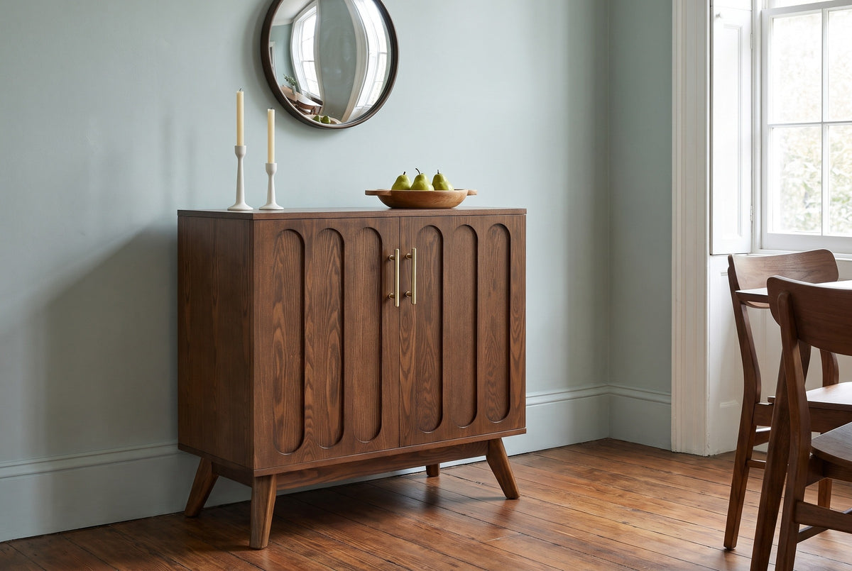 Ruvo walnut-finish cabinet with candlesticks and a bowl of pears under a round mirror against a pale sage-blue wall in a Charleston dining room with heart-pine floors