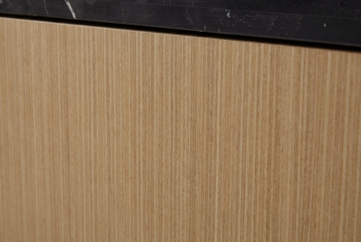 Close-up of the honey-tan eucalyptus veneer on the Samassi nightstand: a fine straight striped grain under the black stone top