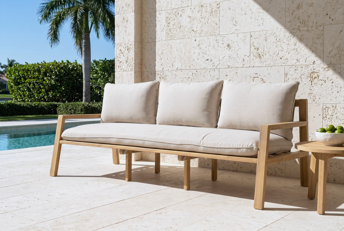 The Sambuca acacia outdoor sofa with beige cushions by a pool on a Naples travertine terrace, a cream coral stone wall and a royal palm behind (side table not included)