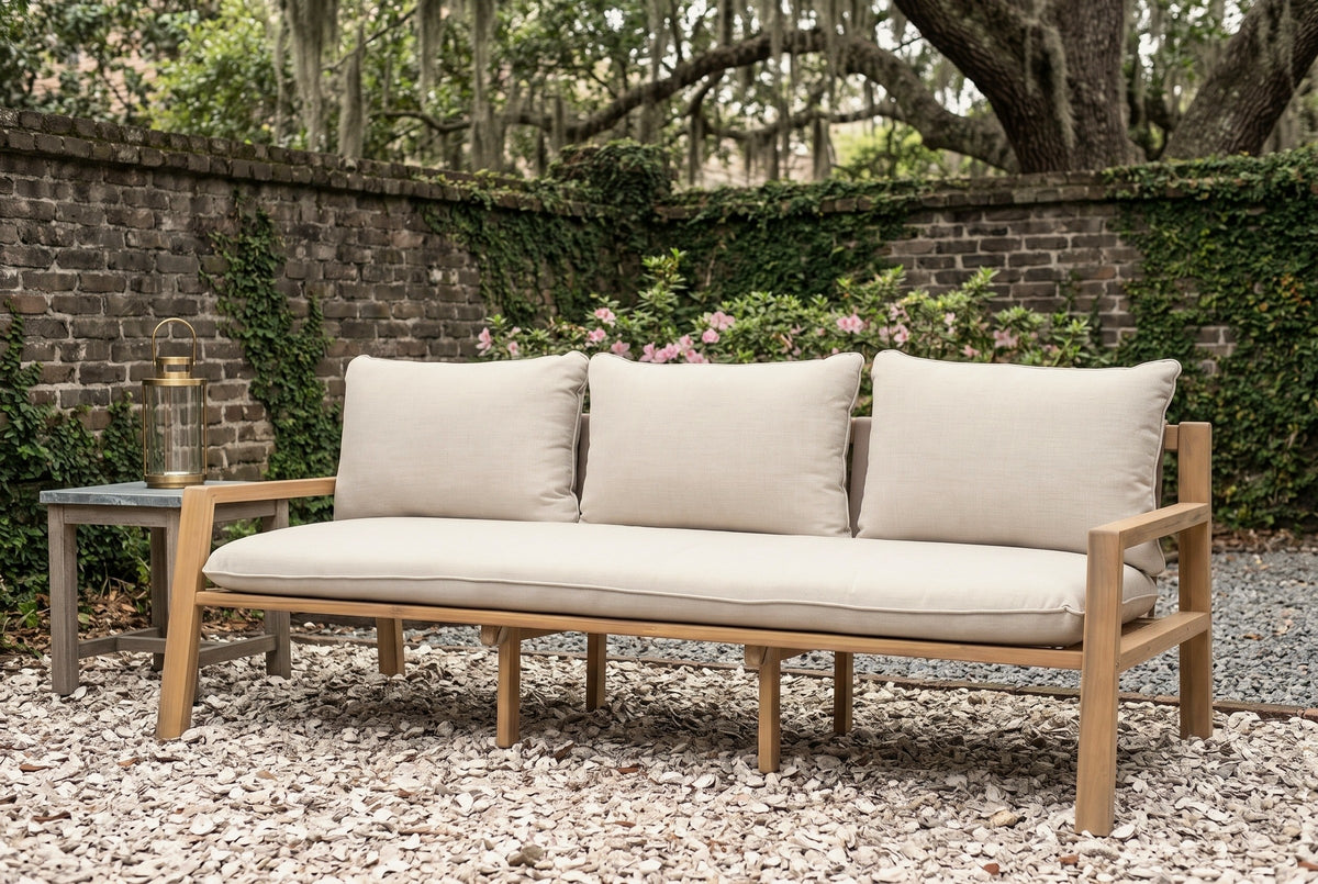 The Sambuca acacia outdoor sofa on oyster shell gravel in a Savannah walled garden, an old brick wall with creeping fig and azaleas behind (side table and lantern not included)