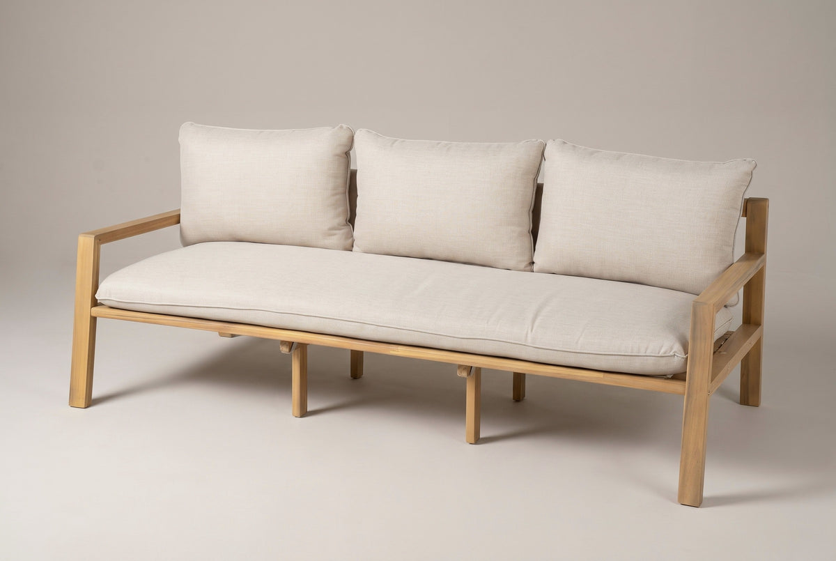 The Sambuca slim-arm acacia outdoor sofa with one long beige seat cushion and three back cushions, three-quarter view on a light studio backdrop