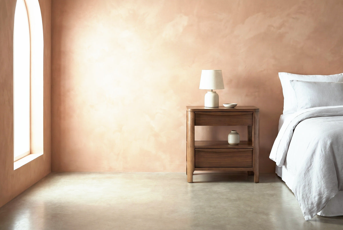 Sanluri walnut two-drawer nightstand with a ceramic lamp beside a bed in a Los Angeles bungalow bedroom with a terracotta limewash wall and an arched window
