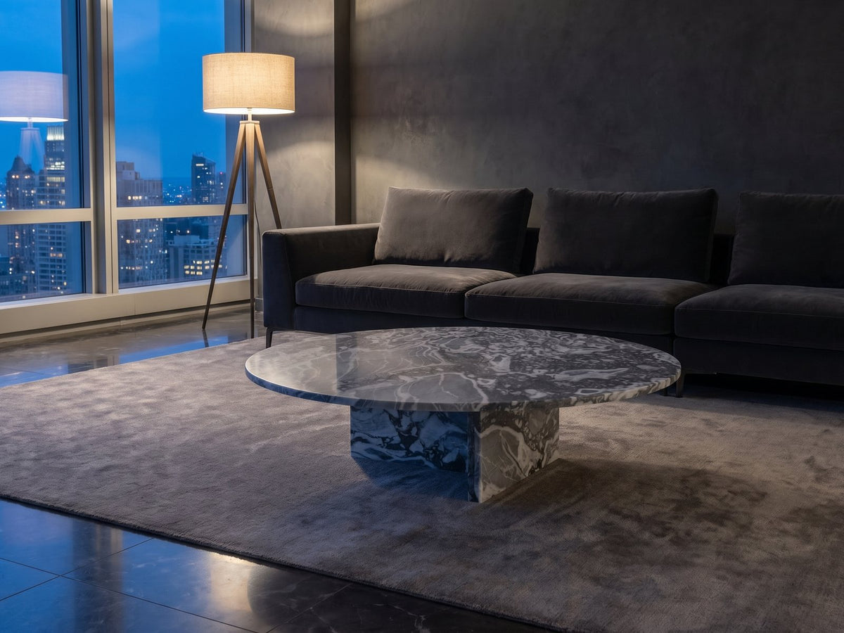 Saturnia Blue-Grey Marble Coffee Table on a wool rug in front of a velvet sofa in a city penthouse at blue hour