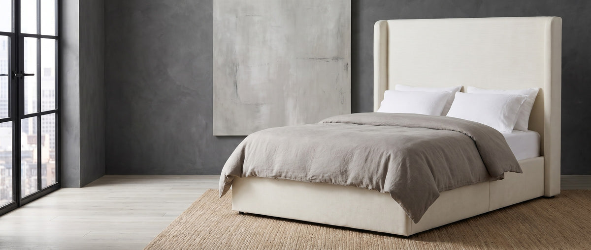 Scanno ivory canvas wingback bed with a tall plain headboard against a charcoal limewashed wall in a Chicago greystone loft, a black steel window at the left