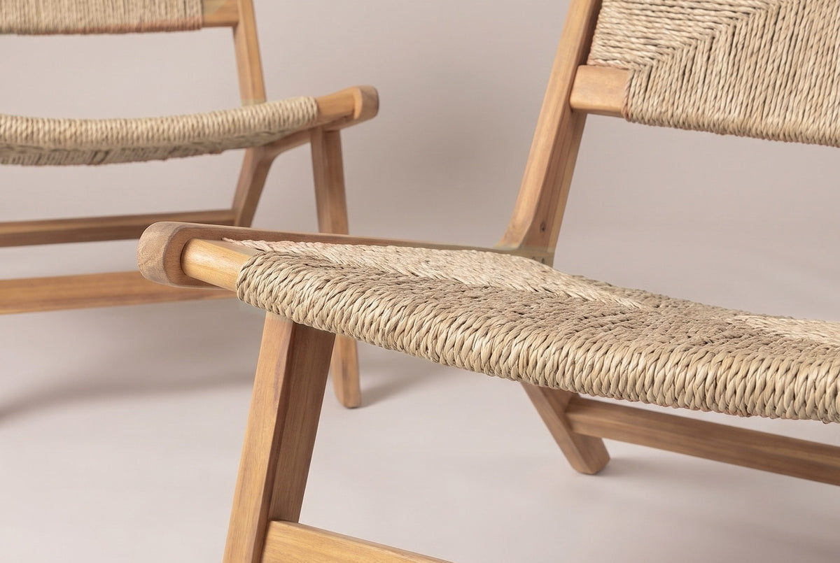 Two Scopello lounge chairs close up: the woven seat and back of the nearer chair, its rounded acacia front lip, a splayed front leg and the low stretcher
