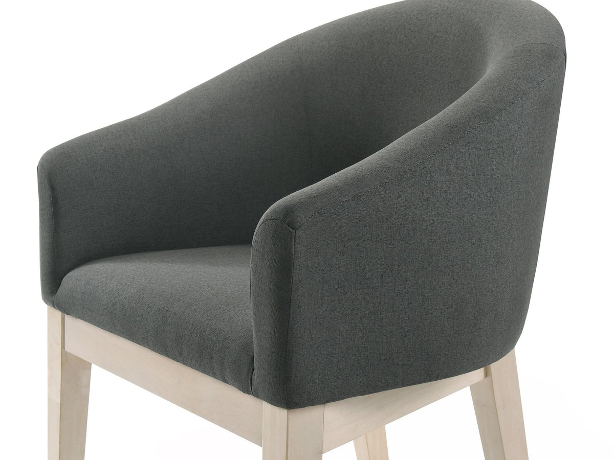 Close-up of the Seminara 80-Inch Oval Fluted Pedestal Dining Set with 6 Chairs: the curved barrel back and low arms of a chair in charcoal-grey fabric on pale wood legs