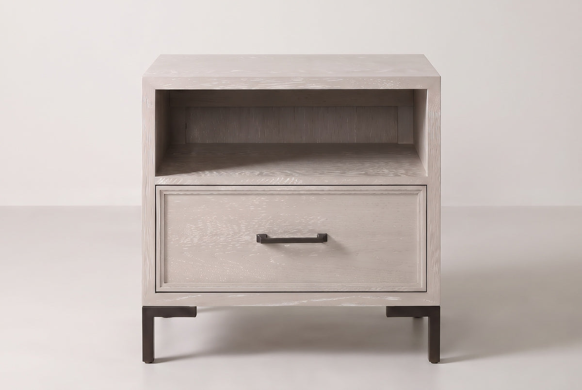 The Sennori nightstand in pale cerused oak, front view on a light studio backdrop: open shelf, one drawer and four bronze legs