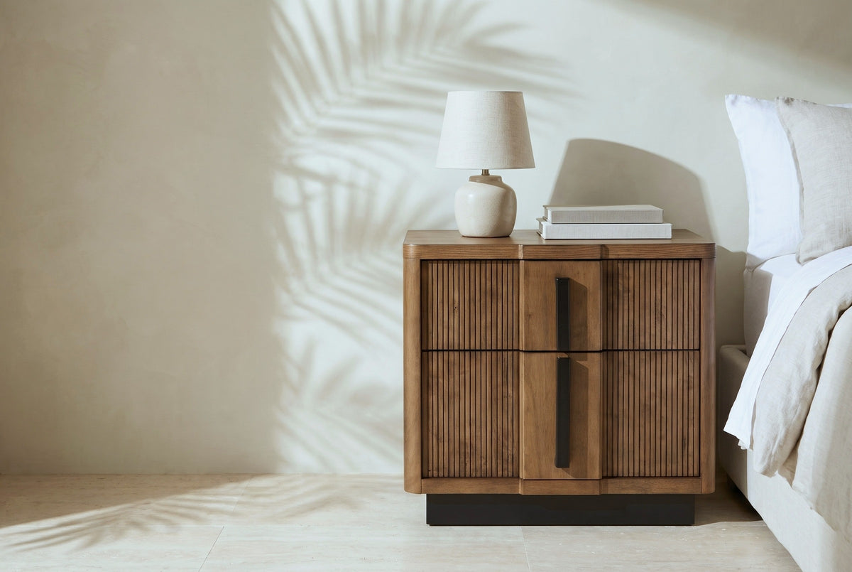 Senorbi reeded ash brown nightstand with a ceramic lamp beside a bed in a Los Angeles bedroom with an ivory plaster wall and palm shadows