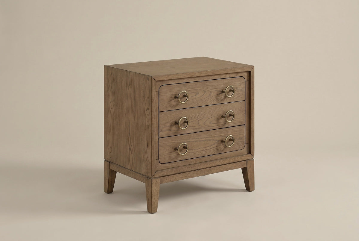 The Serramanna three-drawer nightstand in latte elm veneer with antique-brass ring pulls, three-quarter view on a light studio backdrop