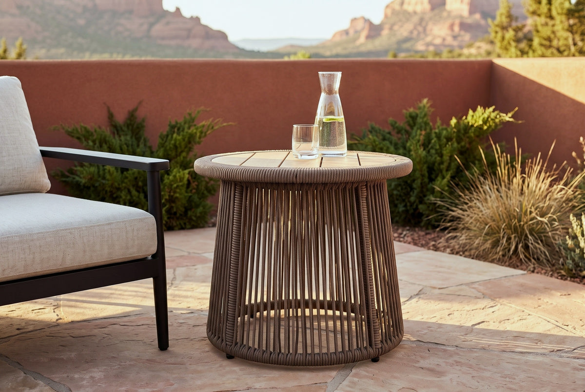 Siculiana rope side table with a glass carafe of water and a glass beside a black-frame lounge chair on a sandstone patio in Sedona, a rust-red stucco wall and the red rocks behind (chair and decor not included)