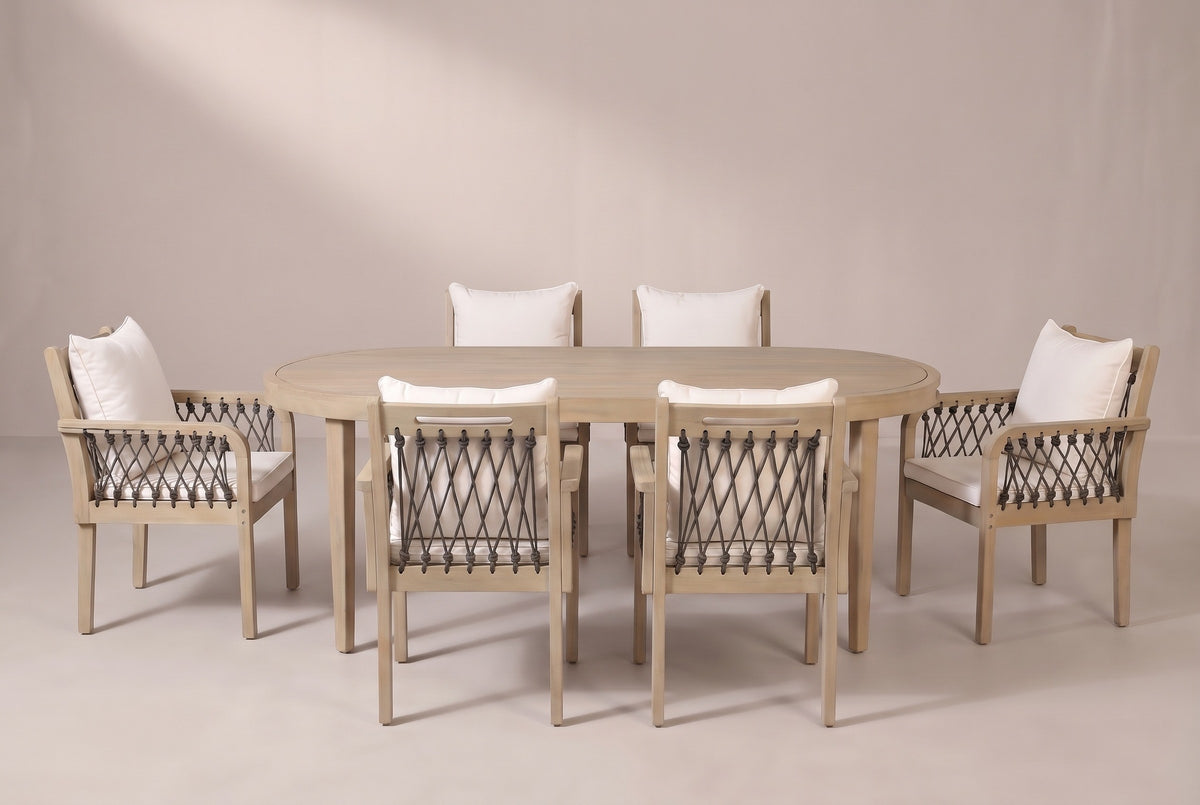 The Siracusa 7-piece dining set in light teak: an acacia oval table and six armchairs with dark gray rope and ivory cushions on a light studio backdrop