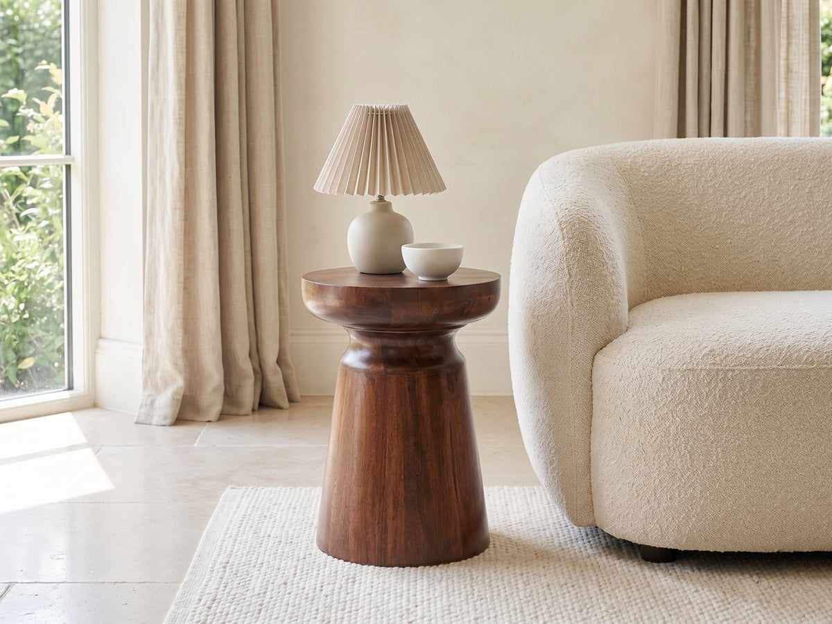 Specchia Brown Mango Cone Pedestal Side Table with a lamp and a ceramic bowl beside a cream boucle armchair in a bright plaster room
