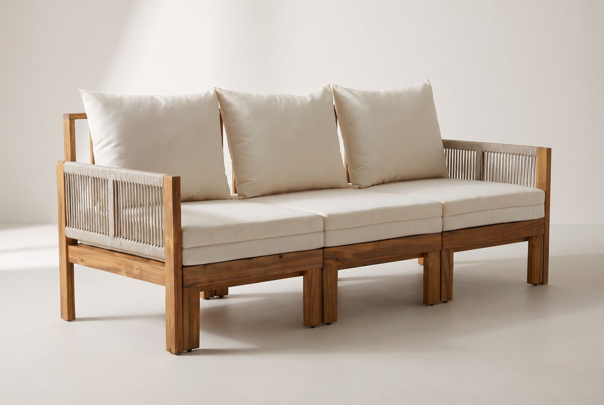 The Sperlinga three-seat sofa in natural acacia with rope arms and ivory-beige cushions, three-quarter view on a light studio backdrop