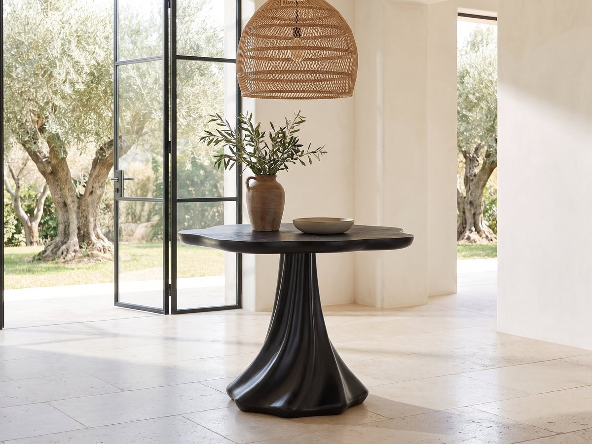 Spilimbergo Black Fiberglass Twisted Petal Pedestal Dining Table in a sunlit villa dining area with olive trees outside