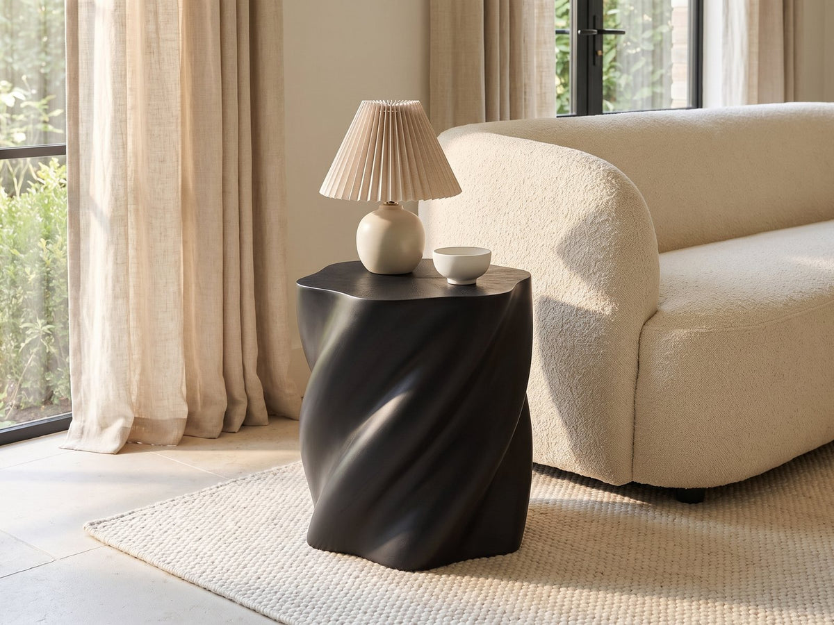 Spilimbergo Black Fiberglass Twisted Petal Side Table with a lamp and a ceramic bowl beside a cream boucle sofa in a bright plaster room