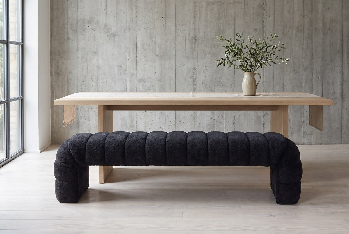 Spoleto black chenille bench pulled up to a long pale oak dining table in a Berlin loft dining room with a raw concrete wall and pale ash floorboards (table not included)