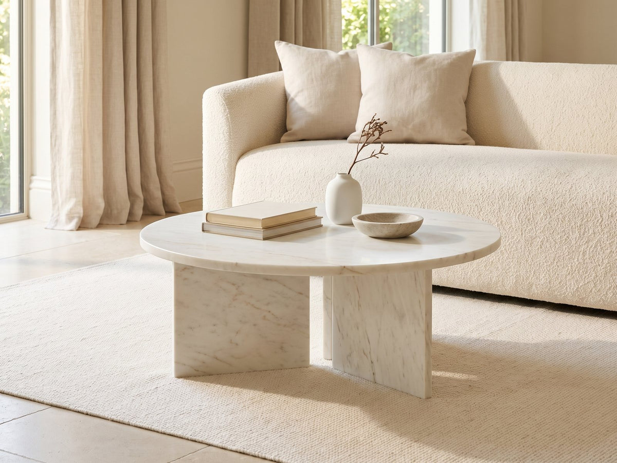 Stintino White Marble Coffee Table styled with books, a vase and a stone bowl in front of a cream sofa in a bright plaster room