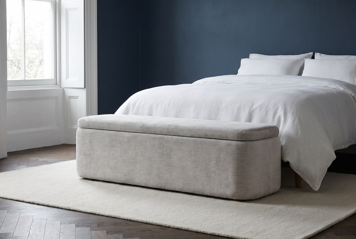Subiaco gray storage bench at the foot of a bed with white linen bedding in a Brooklyn brownstone bedroom with a deep indigo wall and a dark herringbone floor (bed and rug not included)