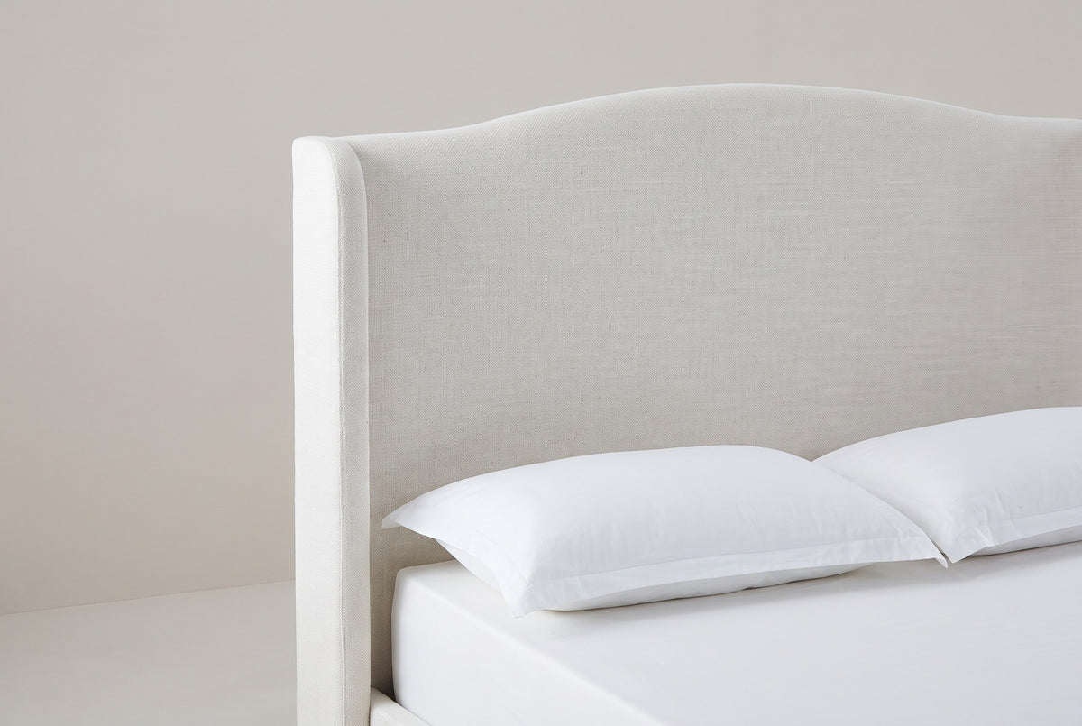 One side of the Sulmona headboard: the camelback top edge sweeping up from the shoulder to the crown, and the rounded-top wing beside the plain flat panel, above a white pillow