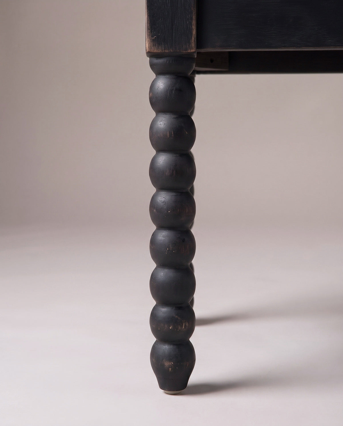 One bobbin leg of the Sutri bench: a small collar under the square corner block, seven round black beads and a tapered foot on the floor