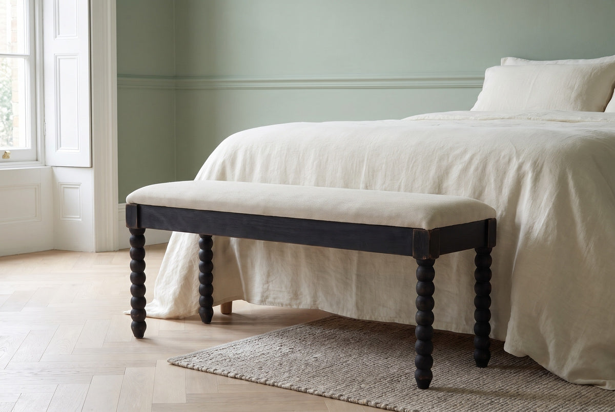 Sutri black bobbin-leg bench at the foot of a bed with ivory linen bedding in a Brooklyn brownstone bedroom with a sage green wall and a pale herringbone floor (bed not included)