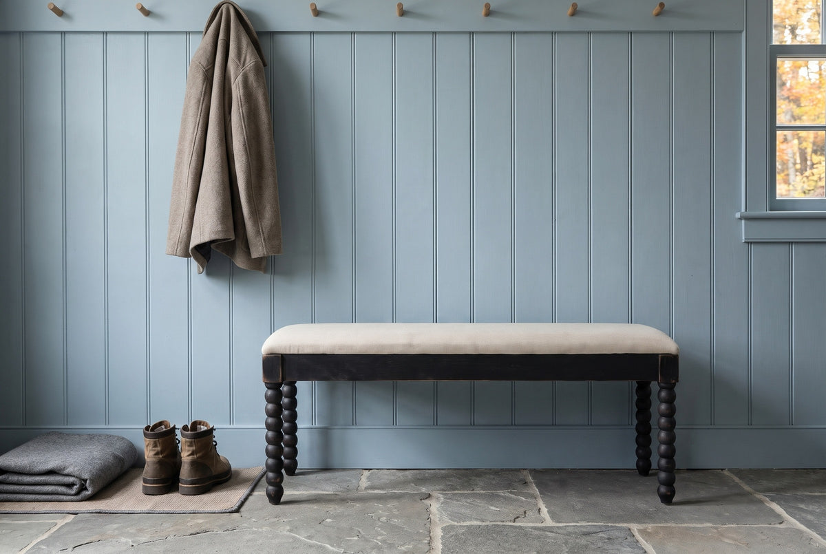 Sutri black bobbin-leg bench against dusty blue board-and-batten panelling in a Hudson Valley mudroom with a bluestone floor, a pair of boots, a folded wool blanket and a coat on a peg