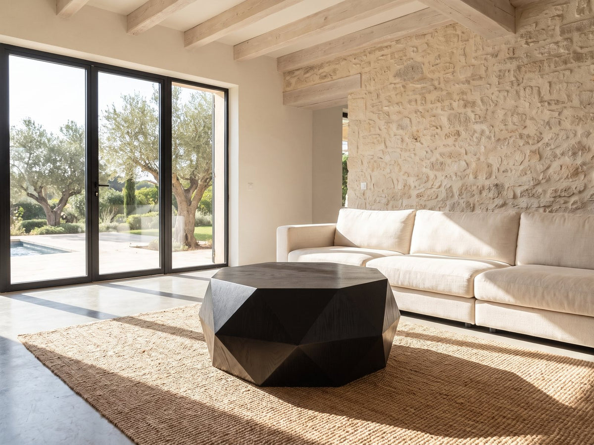 Taranto Black Faceted Drum Coffee Table seen from the side, on a jute rug in front of a linen sofa in a poolside villa