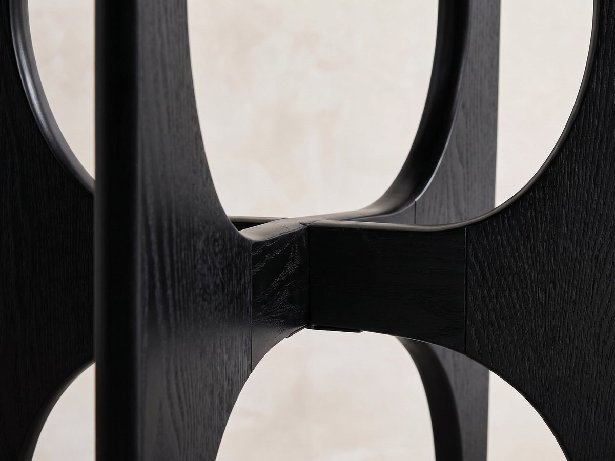 Close-up of the Taviano Black Wood Veneer Round Side Table: the arched panels of the cross base where they meet
