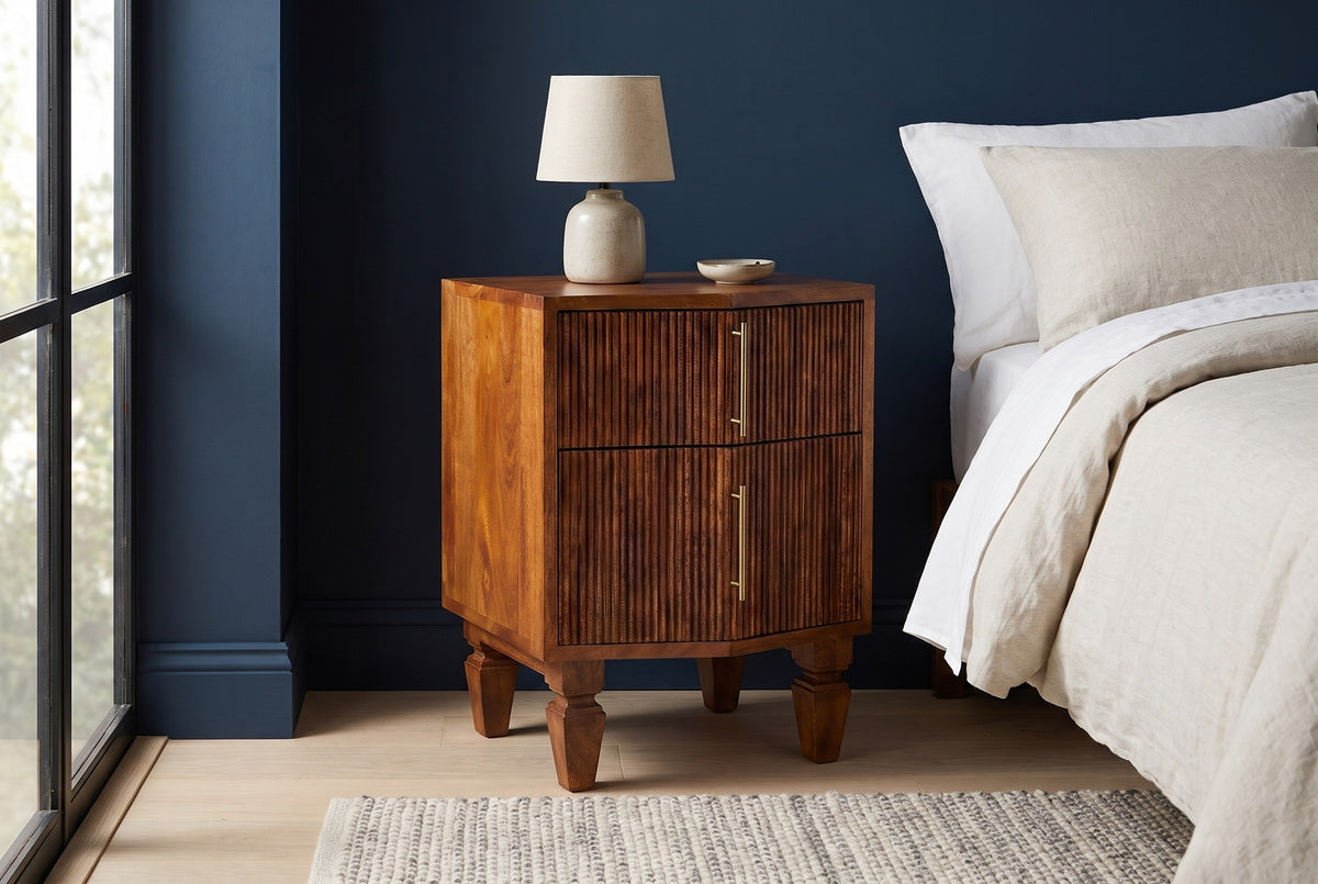 Teulada fluted mango nightstand with a ceramic lamp in a Chicago bedroom with a deep navy wall and a pale oak floor