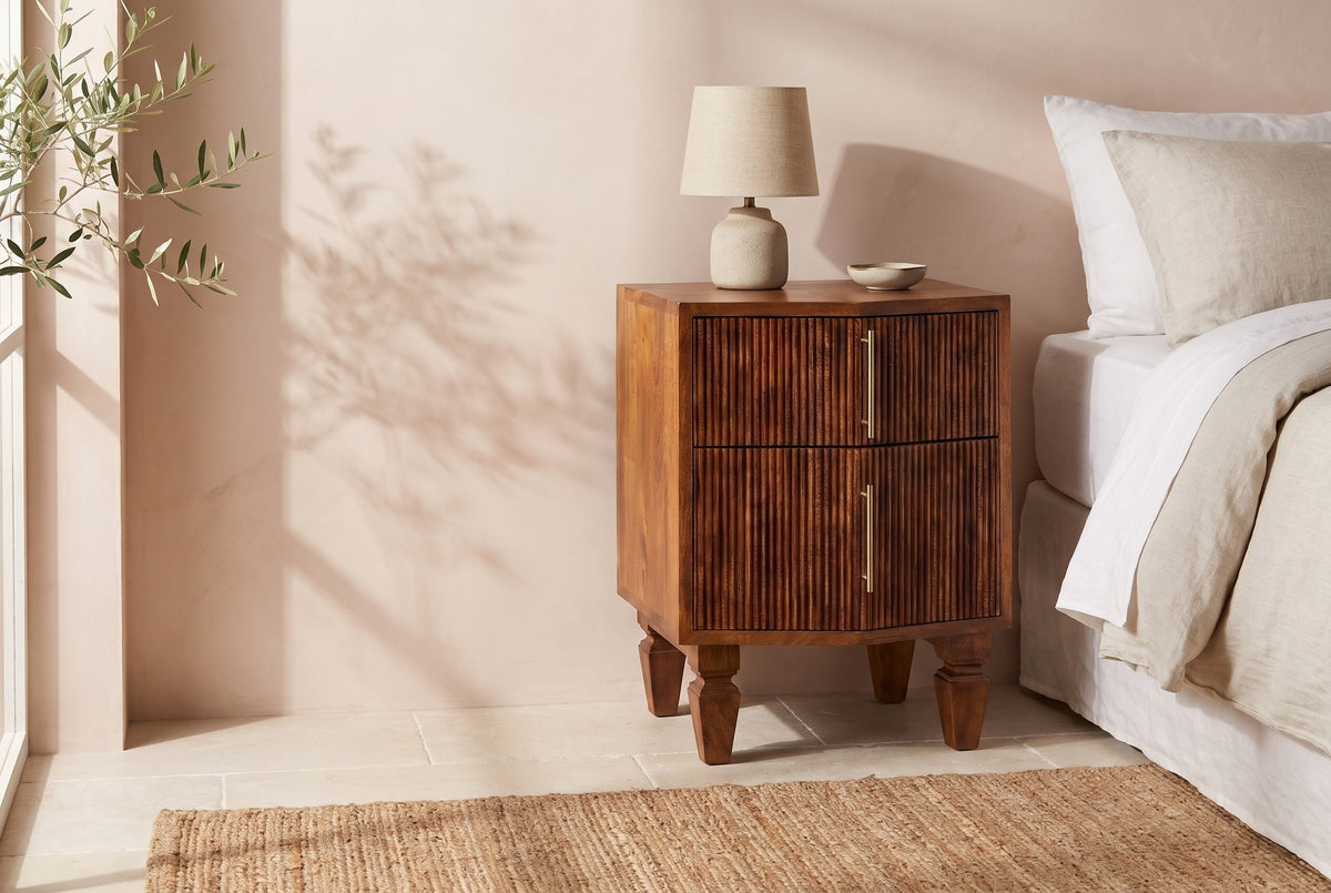Teulada fluted mango nightstand with a ceramic lamp beside a bed in a Santa Barbara bedroom with a blush lime-plaster wall and the shadow of olive branches