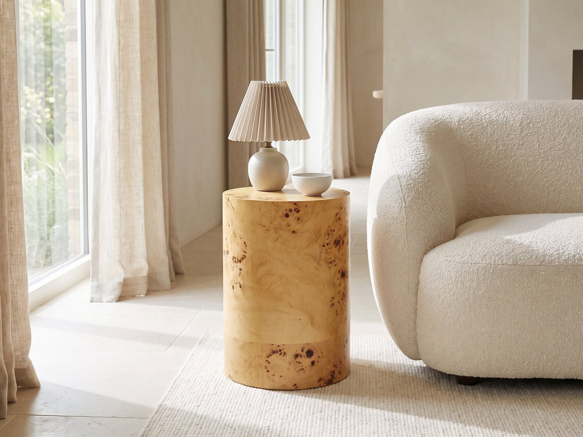 Tiriolo Natural Burl Pillar Side Table with a lamp and a ceramic bowl beside a cream boucle armchair in a bright plaster room