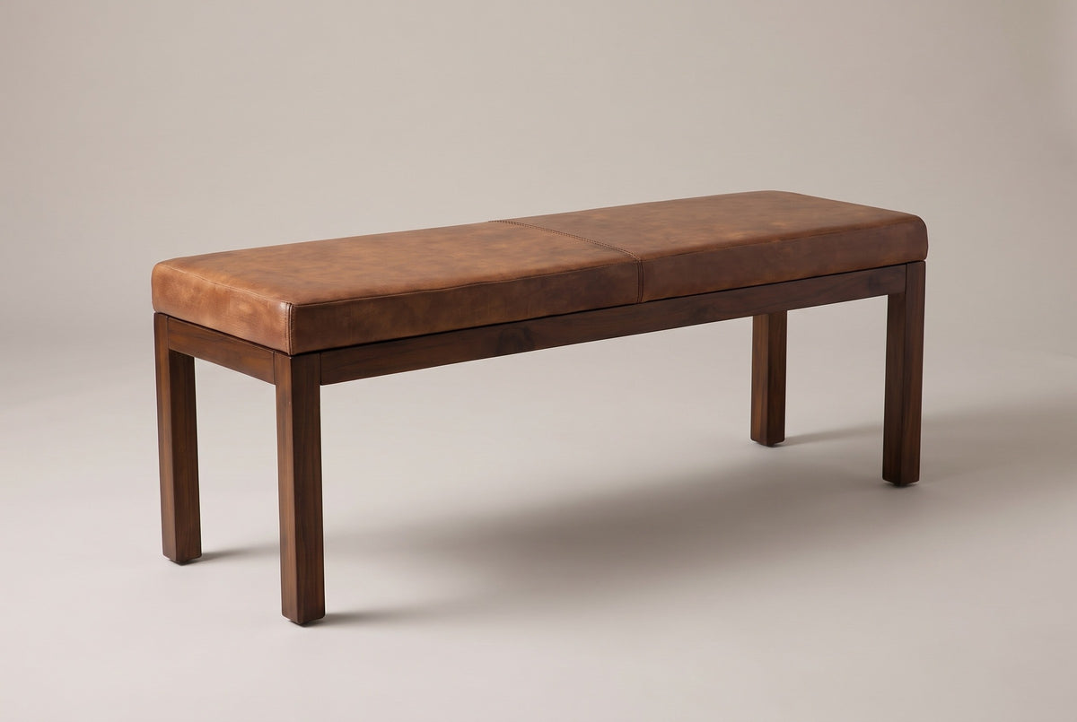 The Todi bench with its antique tan leather cushion, three-quarter view on a light studio backdrop