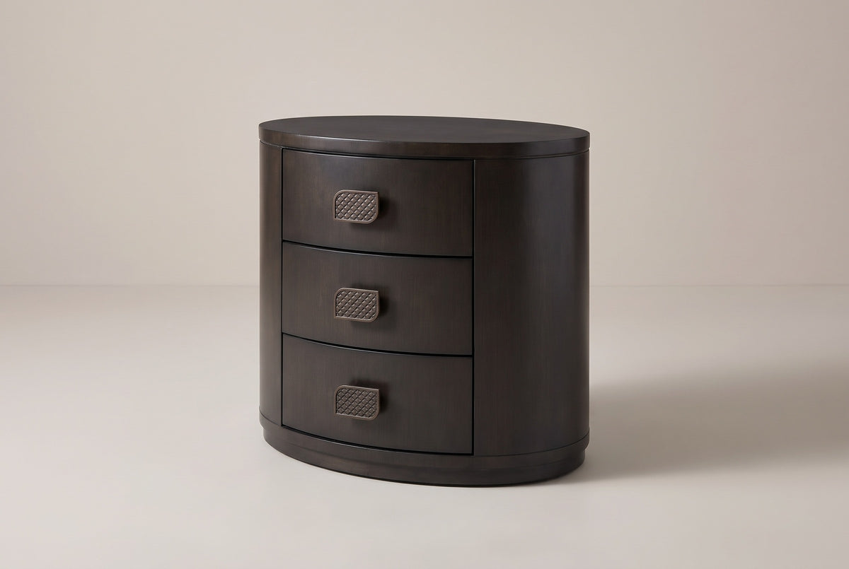 The Tortoli three-drawer oval nightstand in deep espresso eucalyptus veneer, three-quarter view on a light studio backdrop