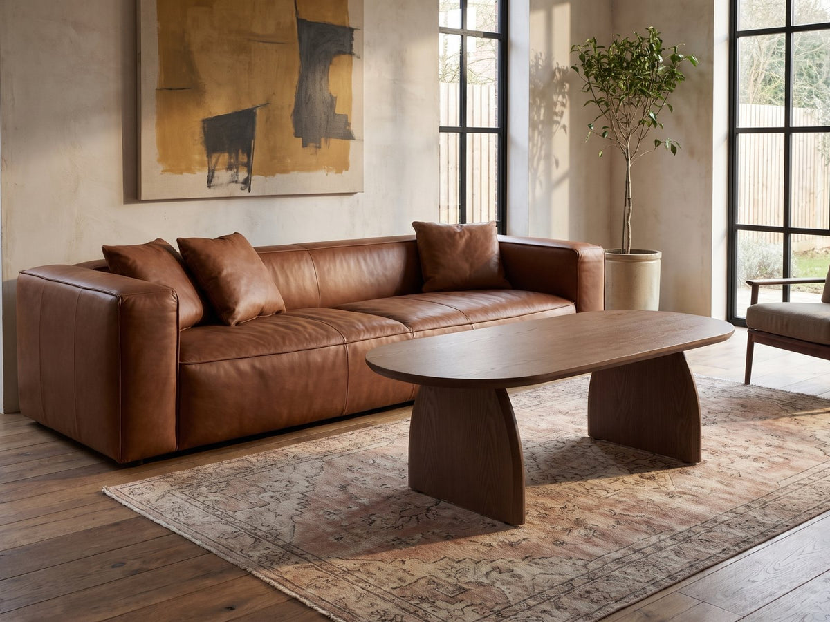 Tortona 47-Inch Oval Walnut-Finish Wood Veneer Coffee Table on a vintage rug in front of a leather sofa in an industrial loft