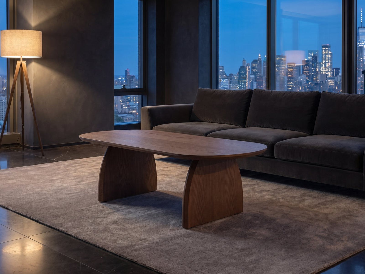Tortona 47-Inch Oval Walnut-Finish Wood Veneer Coffee Table on a wool rug in front of a velvet sofa in a city penthouse at blue hour
