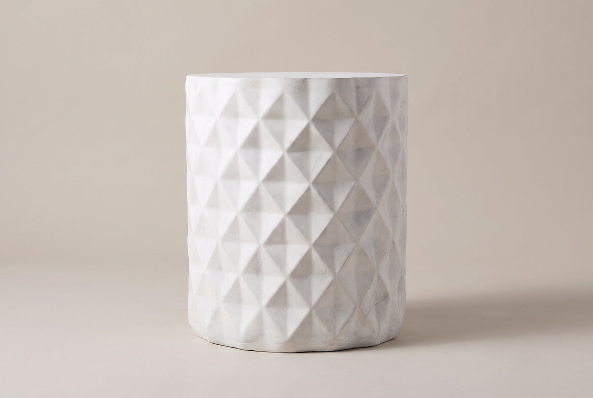 The Tortorici side table seen straight from the side: an upright antique white drum with staggered diamond facets